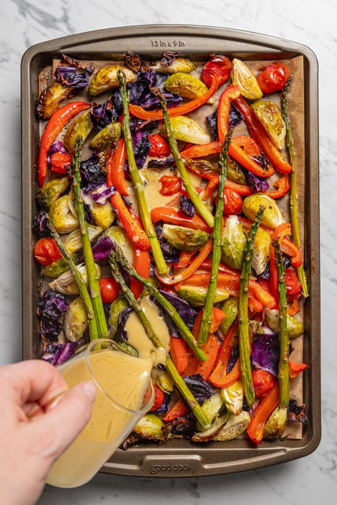 Pouring the dressing over the veggies in the baking sheet. 