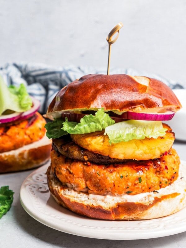 A grilled salmon burger on a plate with another behind it being topped with red onion and lettuce.