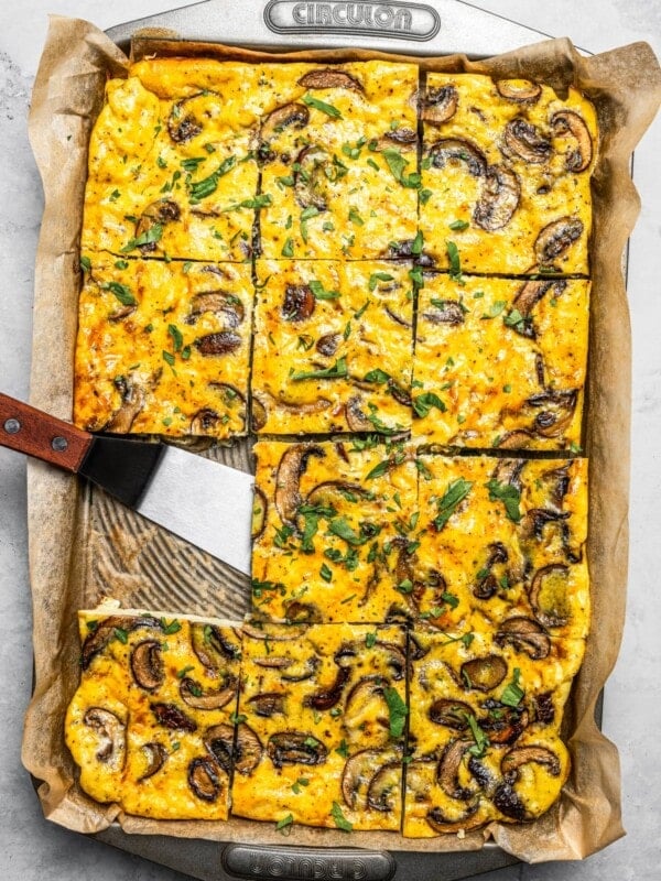 Picking up a slice of sheet pan eggs out of a pan with a spatula.