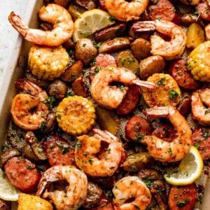 shrimp, potatoes, sausages, and corn arranged on a sheet pan and garnished with a few lemon slices.