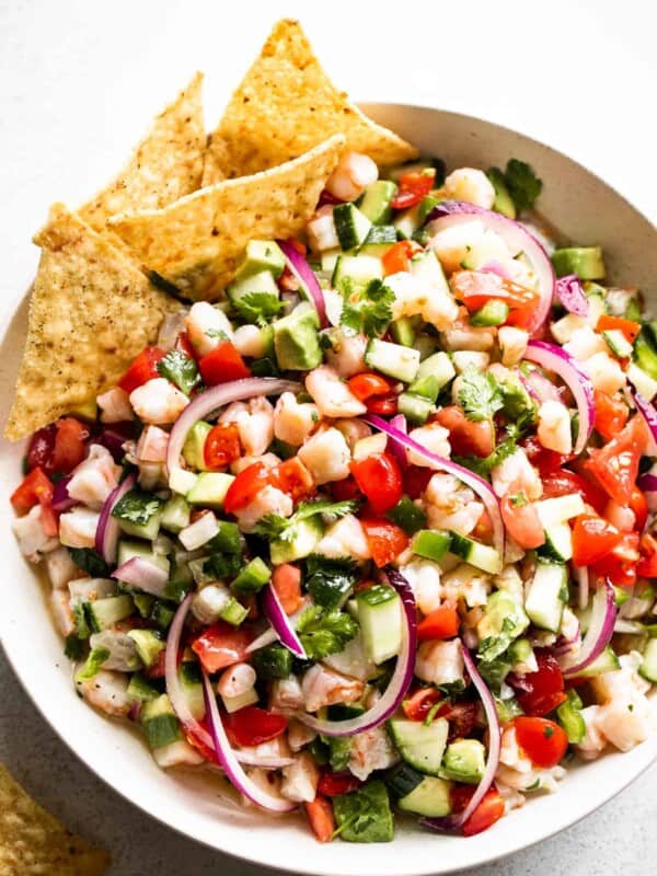 overhead shot of a white bowl with shrimp ceviche that includes diced tomatoes, diced avocado, diced shrimp, diced cucumbers, red onions, and jalapenos.