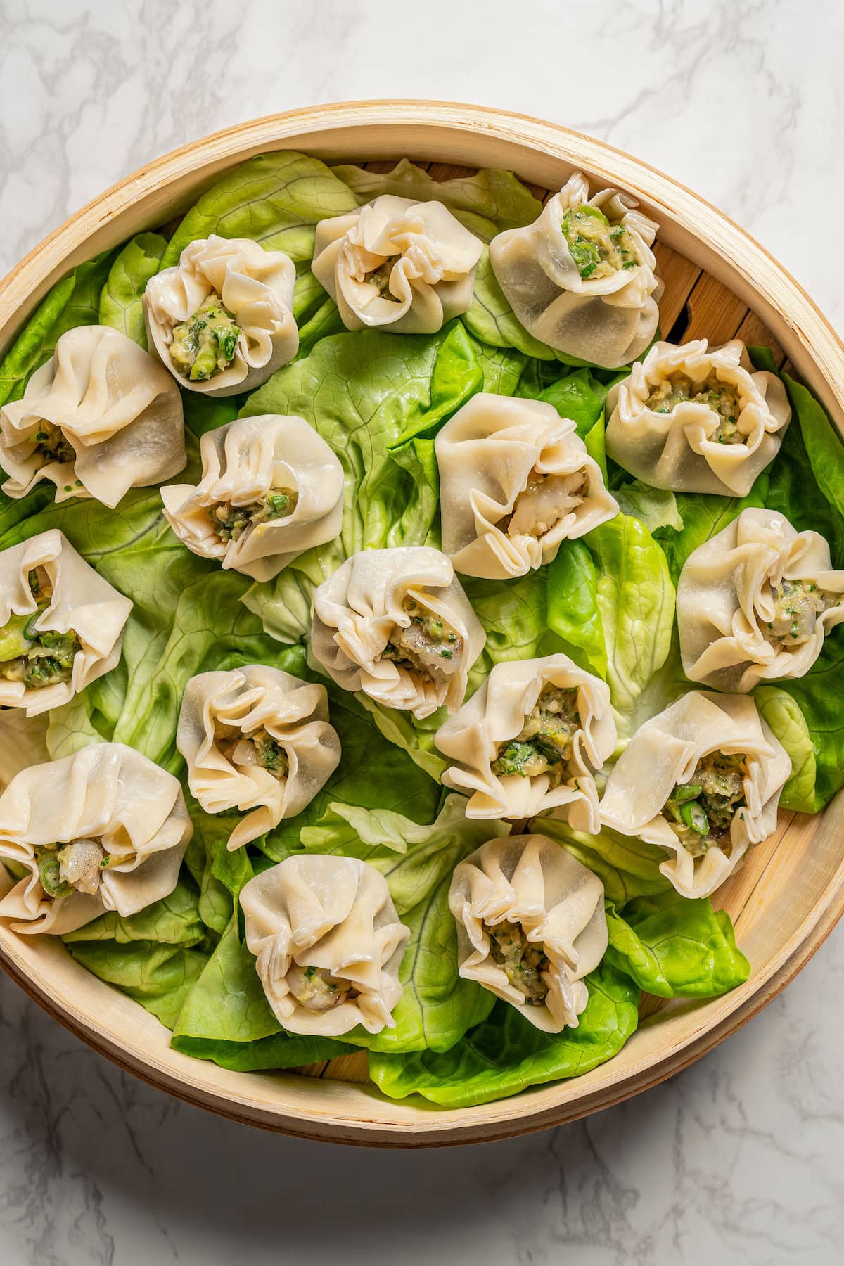 Overhead view of shrimp shumai on top of lettuce leaves inside the bamboo steamer basket.