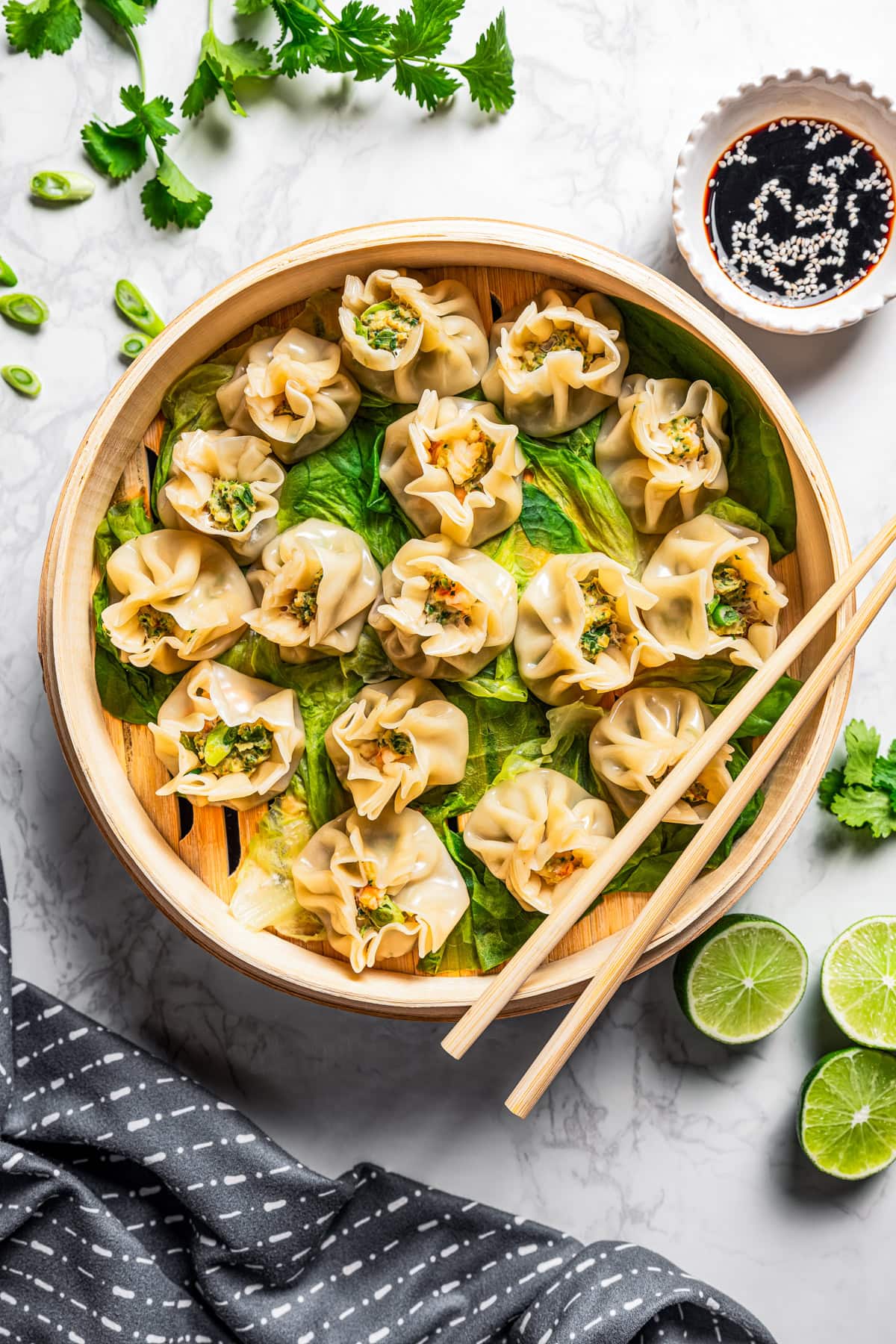 An overhead view shows shrimp shumai arranged on top of lettuce leaves inside the bamboo steamer, with a pair of chopsticks resting on the edge of the basket.