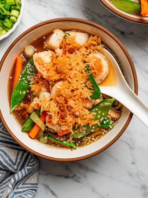 Overhead image of a soup bowl filled with broth, scallops, shrimp, and veggies, and topped with fried rice.