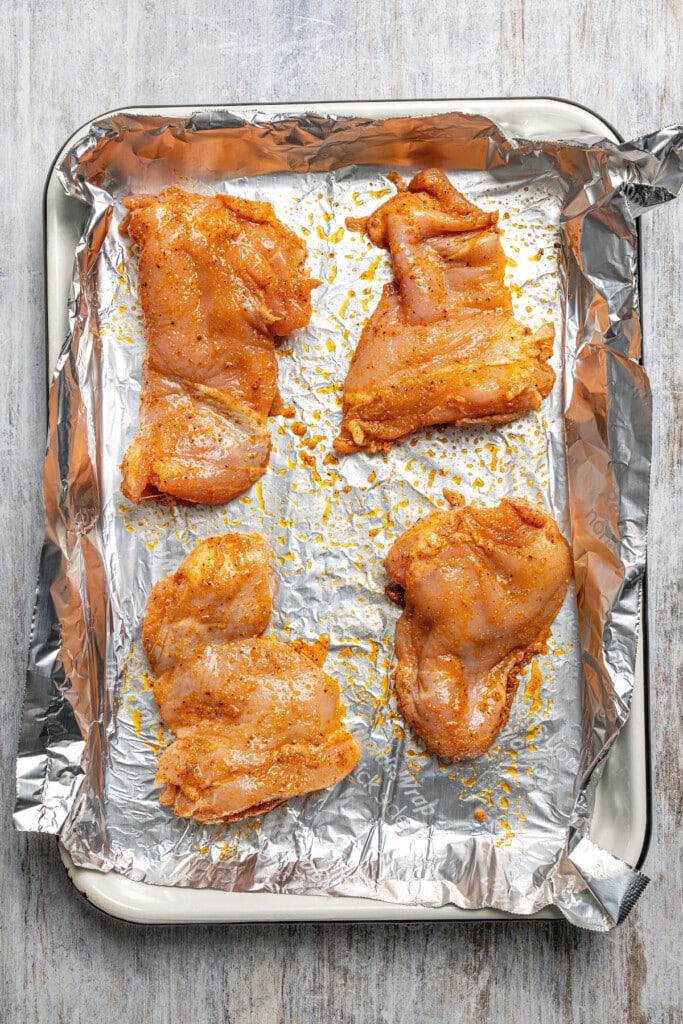 Arranging seasoned chicken thighs on a sheet pan lined with aluminum foil.