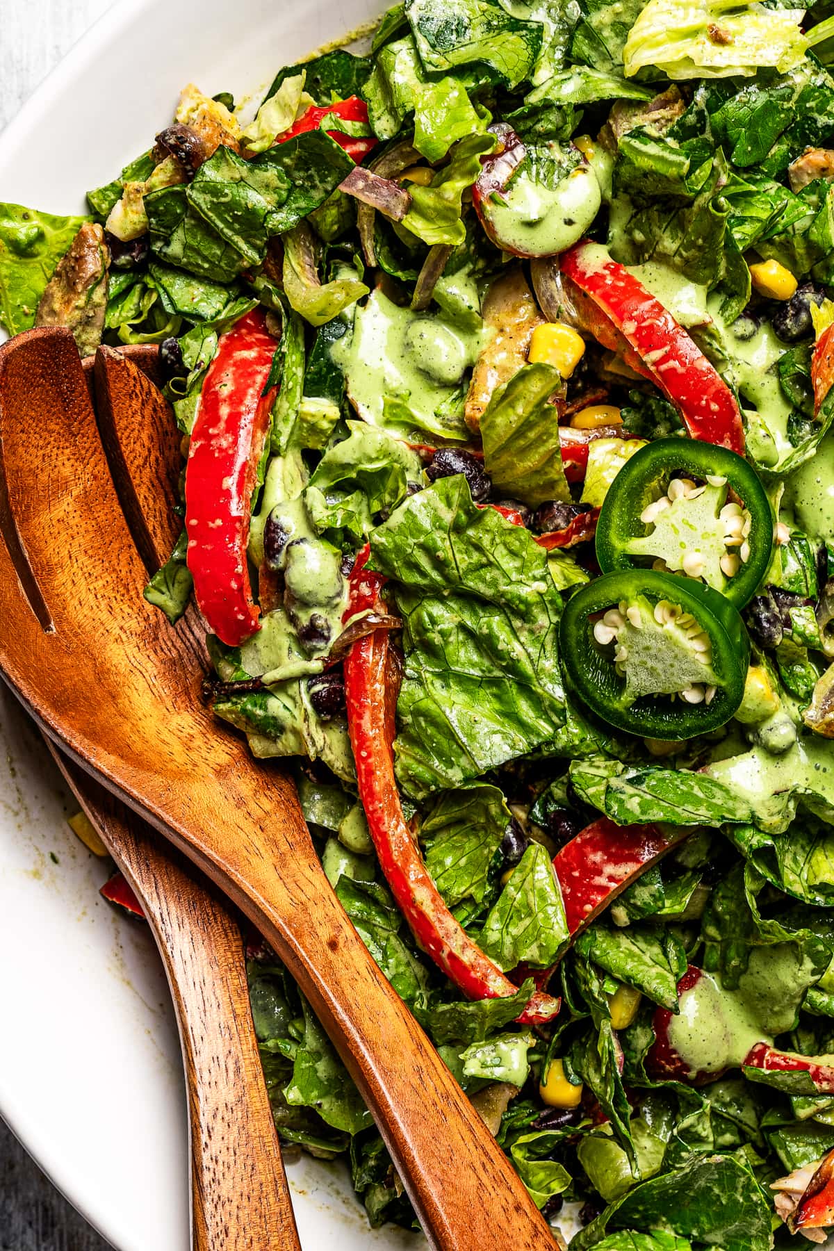 Close-up image of Southwestern Chicken Salad in a salad bowl with wooden serving utensils.