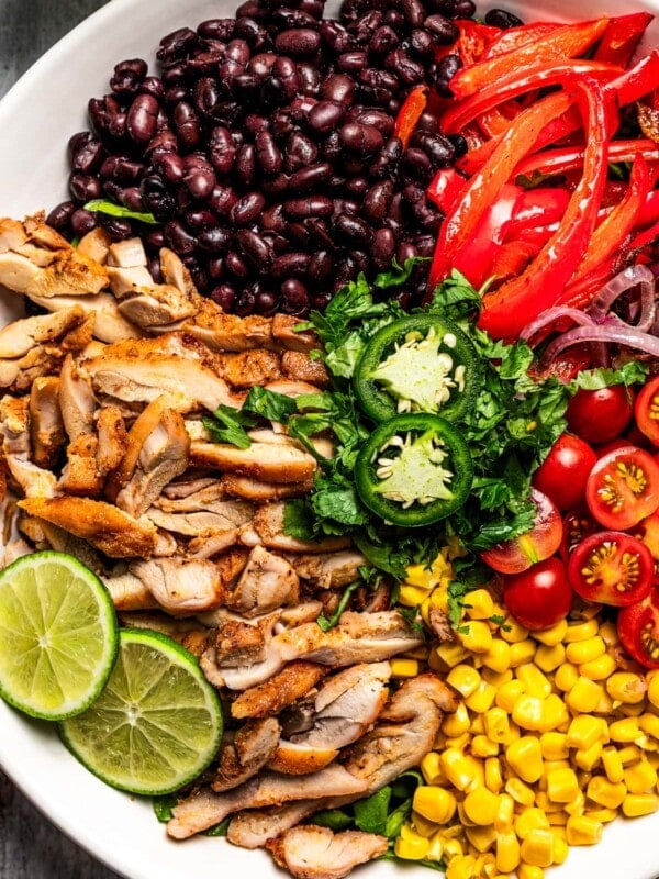 Close-up shot of a bowl with sliced chicken, sliced red bell peppers, black beans, tomatoes, and corn.