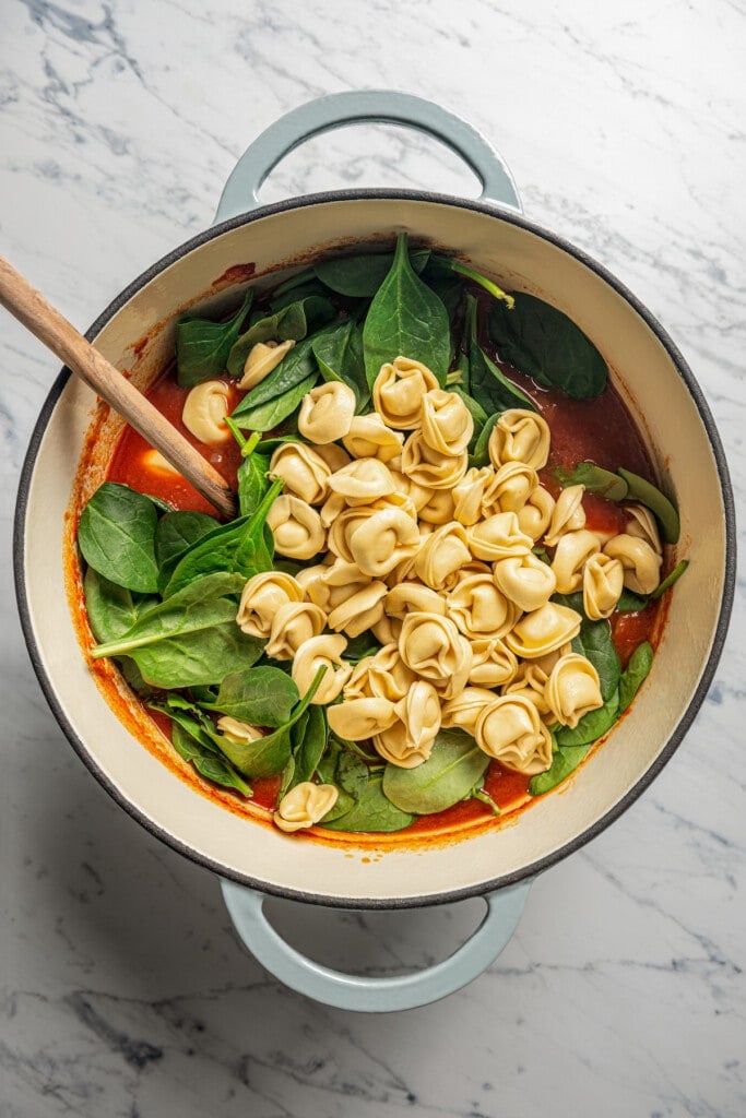 Adding the broth, spinach, and tortellini to the pot. 