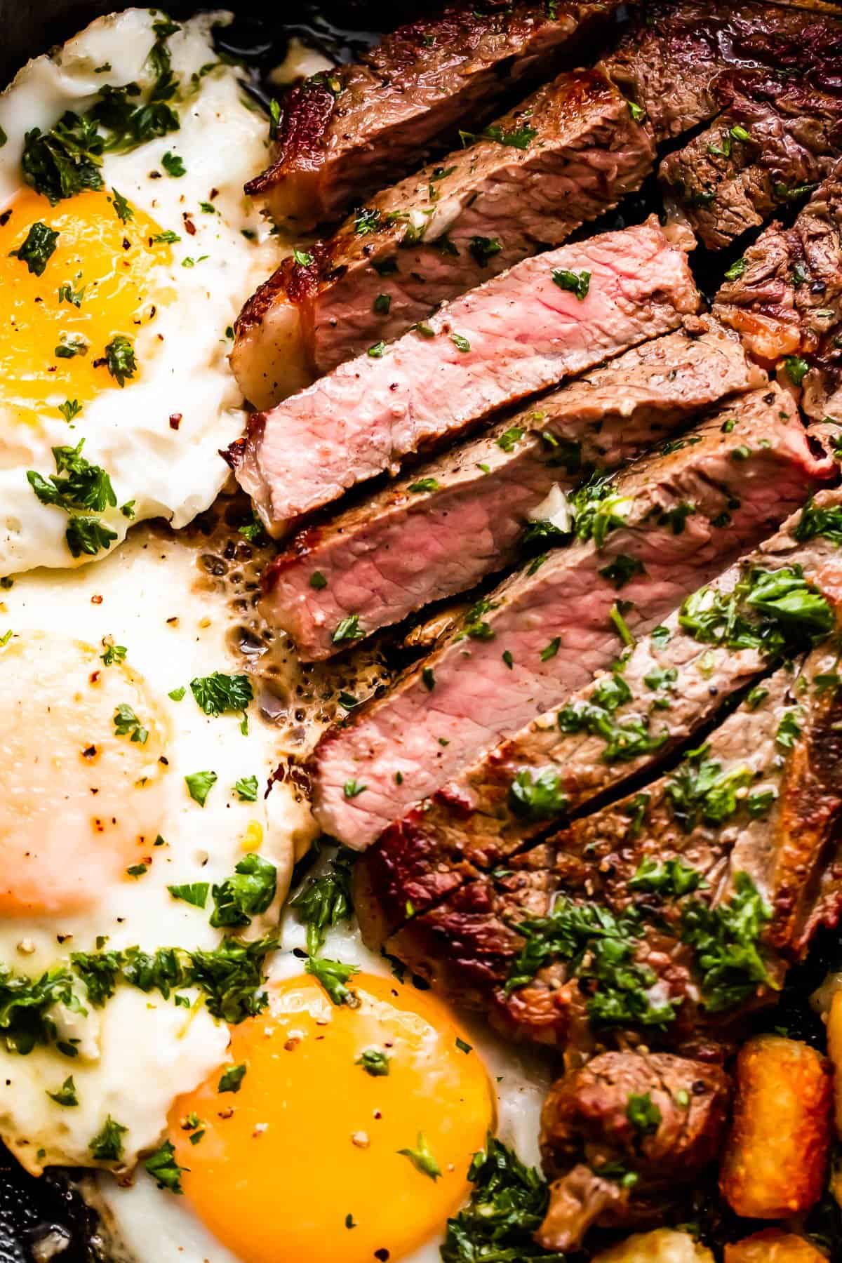 close up shot of t-bone steak cut in slices and served next to three eggs cooked over easy .