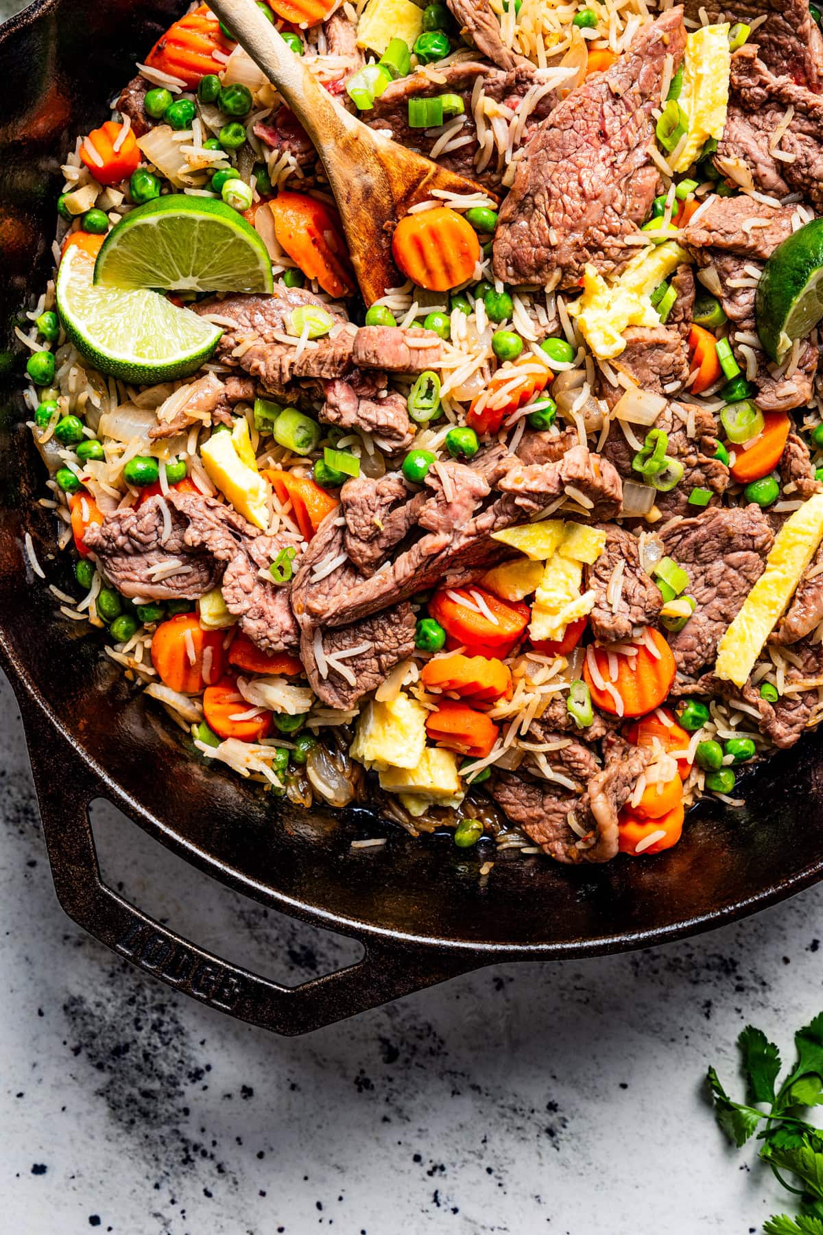 A wooden spoon stirring through steak fried rice in a skillet.