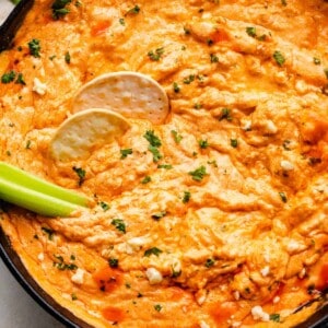 overhead shot of buffalo chicken dip in a cast iron skillet with two crackers and celery sticks in the dip