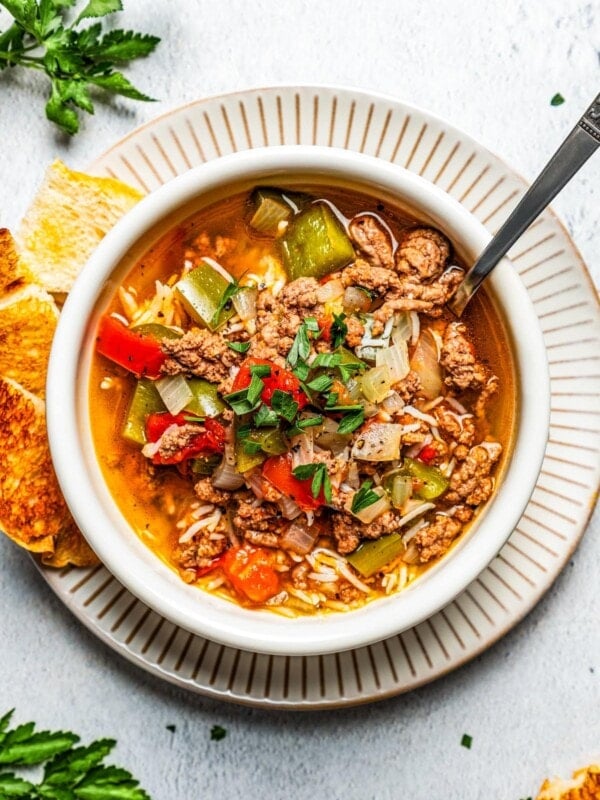 Overhead image of a soup bowl filled with stuffed pepper soup and set on a dinner plate with slices of bread set next to the bowl.