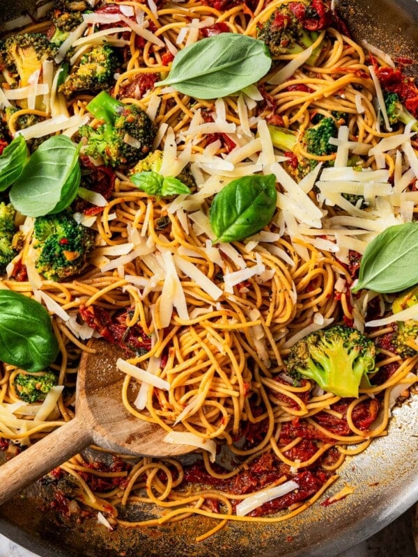 Close-up image of pasta in a skillet tossed with cheese, tomatoes, broccoli, and basil.