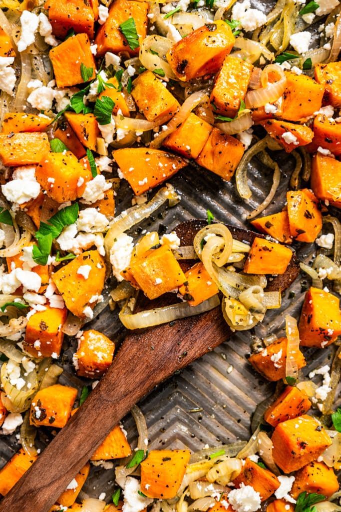 Close-up of a wooden spoon stirring through diced sweet potatoes.