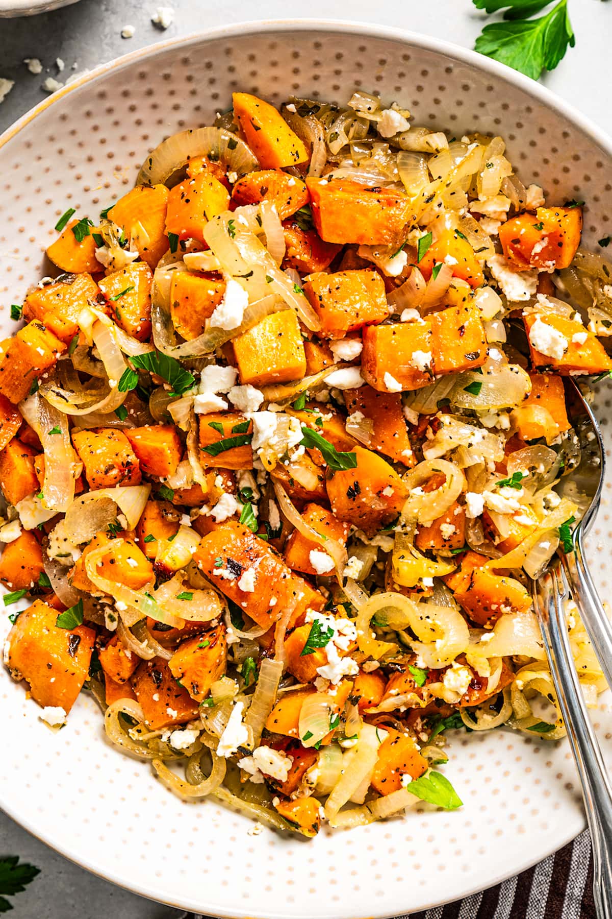 Diced and baked sweet potatoes served in a bowl with onions, herbs, and feta cheese.