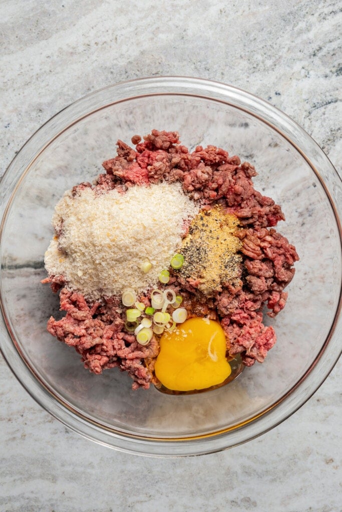 Combining ground beef, egg, panko, soy sauce, salt, black pepper, garlic powder, ground ginger, and the white parts of scallions in a bowl.