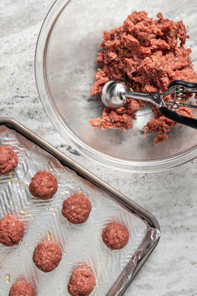 Measuring seasoned meat mixture into 1 1/2 inch meatballs.