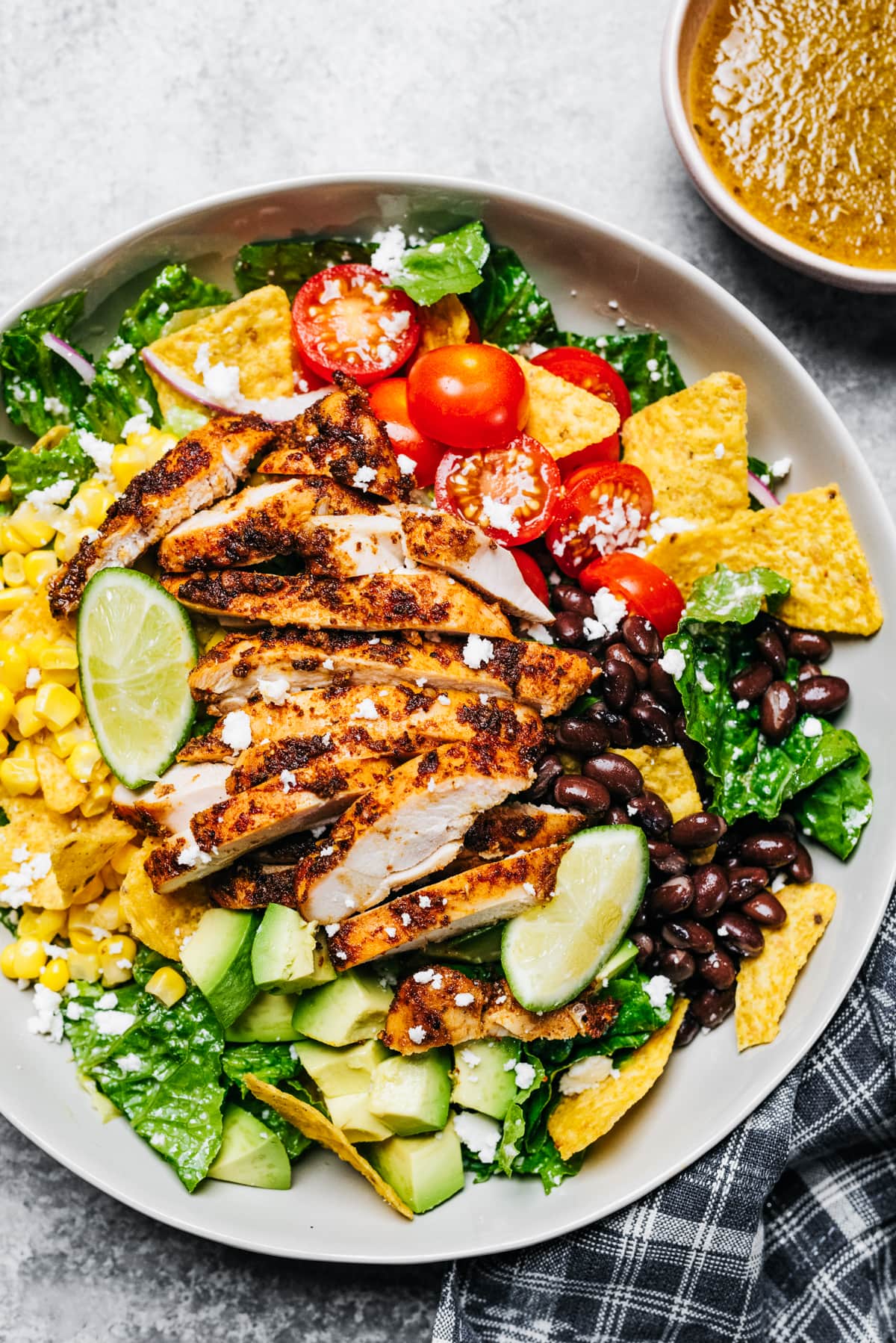 A large bowl with a salad featuring sliced chicken breast, cherry tomatoes, nacho chips, avocado, onions, black beans, and corn.