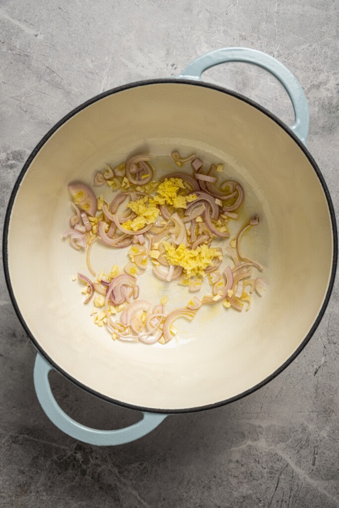 Sauteing shallot, garlic, and ginger in vegetable oil in a soup pot.