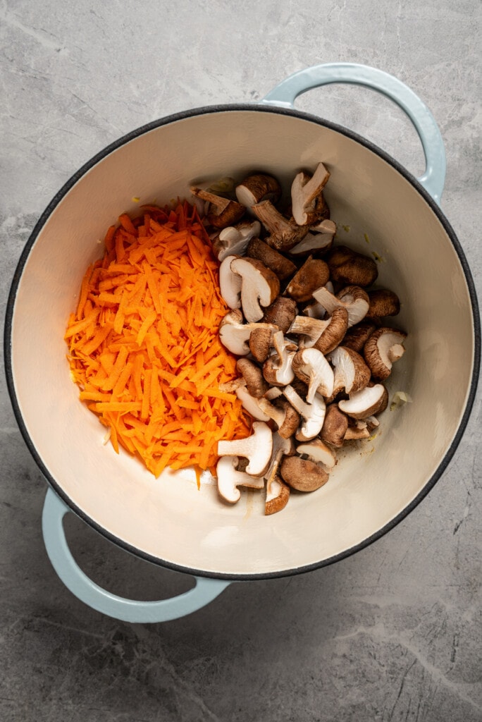 Sauteing carrots and mushrooms with aromatics in a soup pot.