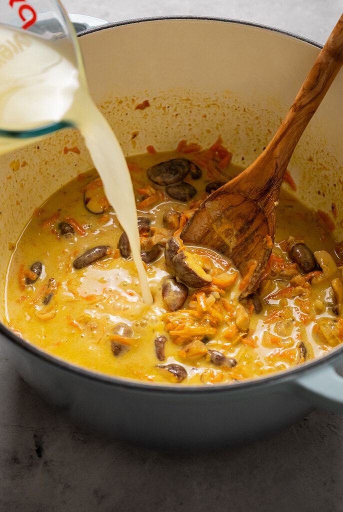 Pouring chicken stock into Thai chicken soup.