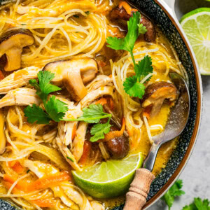 Thai chicken noodle soup served in a bowl and garnished with lime and herbs.