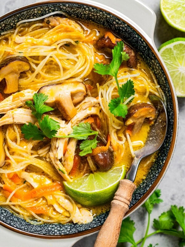 Thai chicken noodle soup served in a bowl and garnished with lime and herbs.