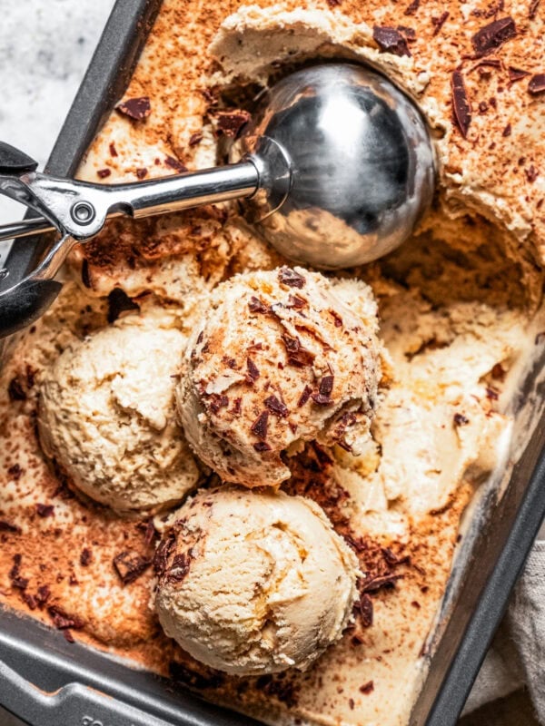 Ice cream in a loaf pan with a scooper inside the pan scooping out balls of ice cream.