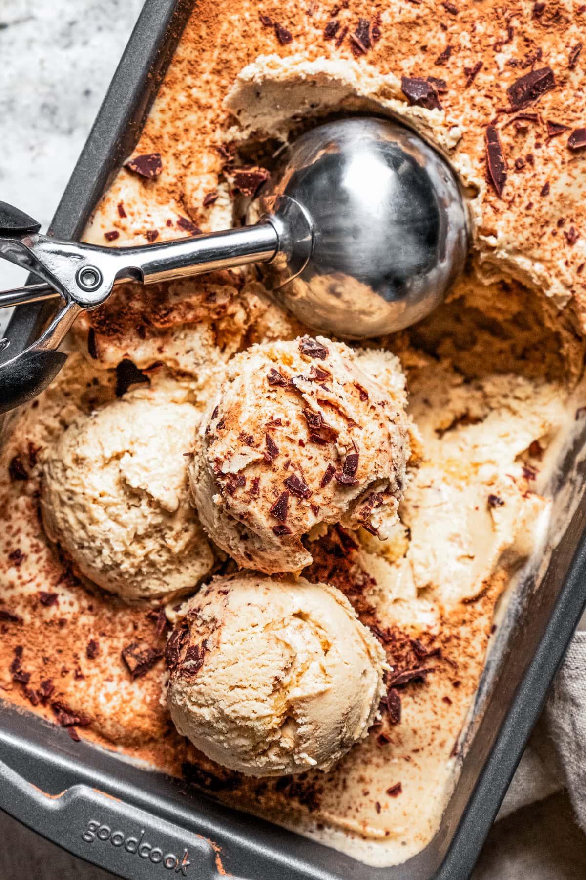 Ice cream in a loaf pan with a scooper inside the pan scooping out balls of ice cream.