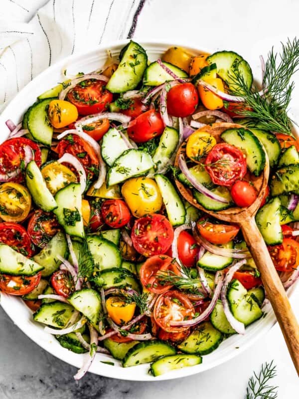 Tomato and cucumber salad in a serving bowl with a wooden spoon.