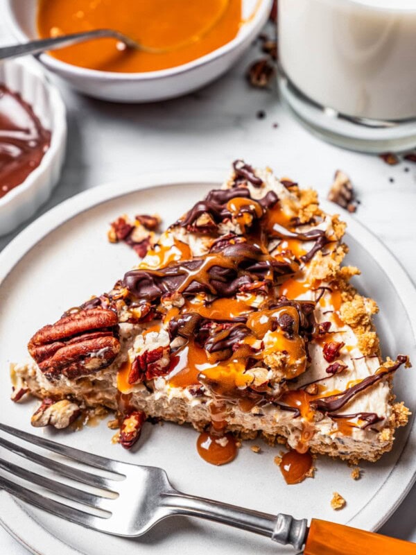 A slice of Turtle pie on a white plate with a fork, next to bowls of toppings.