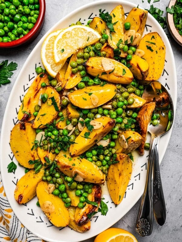 Overhead image of Vesuvio potatoes on a serving platter with lemon slices and serving spoons.