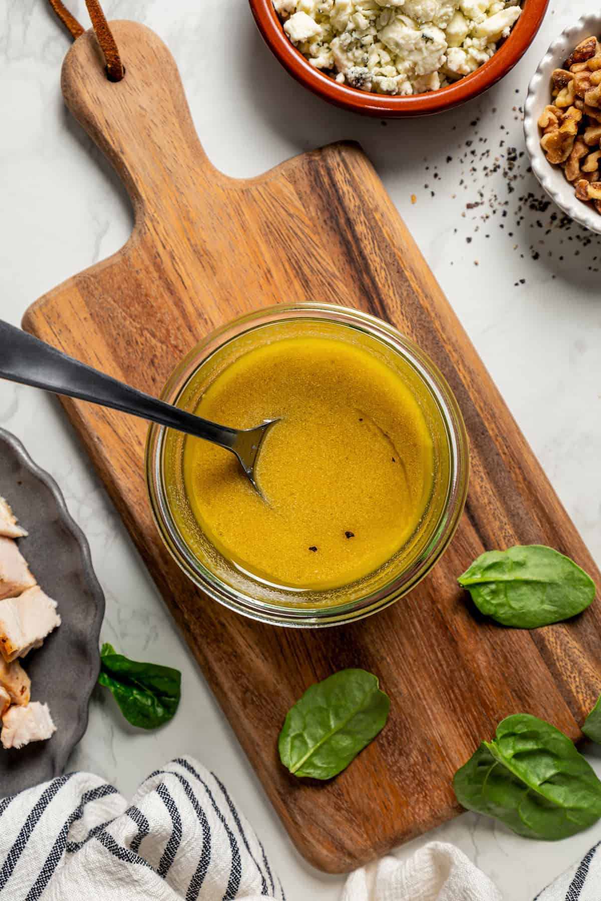 Overhead view of Dijon mustard vinaigrette in a mason jar on top of a wooden cutting board.