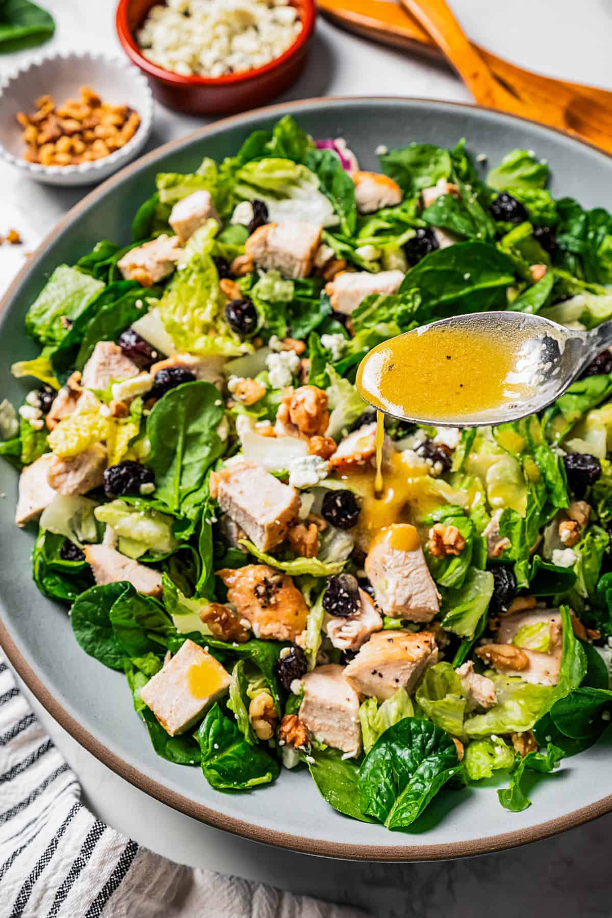 A spoon drizzling Dijon vinaigrette over walnut chicken salad in a large blue bowl.