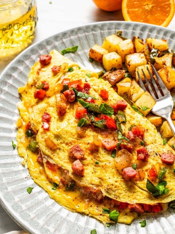 A Western omelette on a plate with breakfast potatoes and a fork.