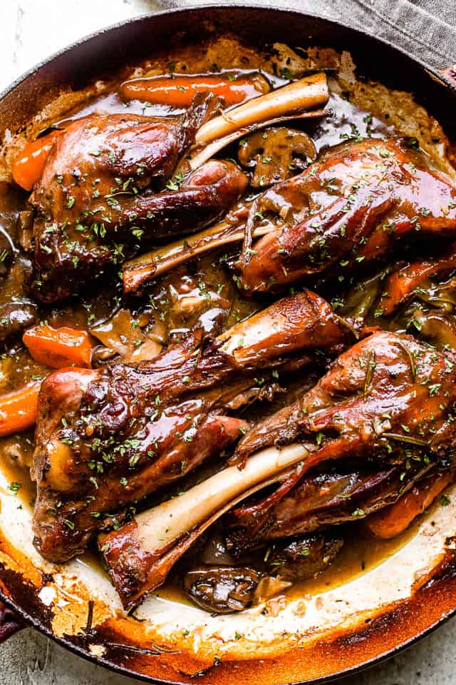 Four cooked lamb shanks in a pan.