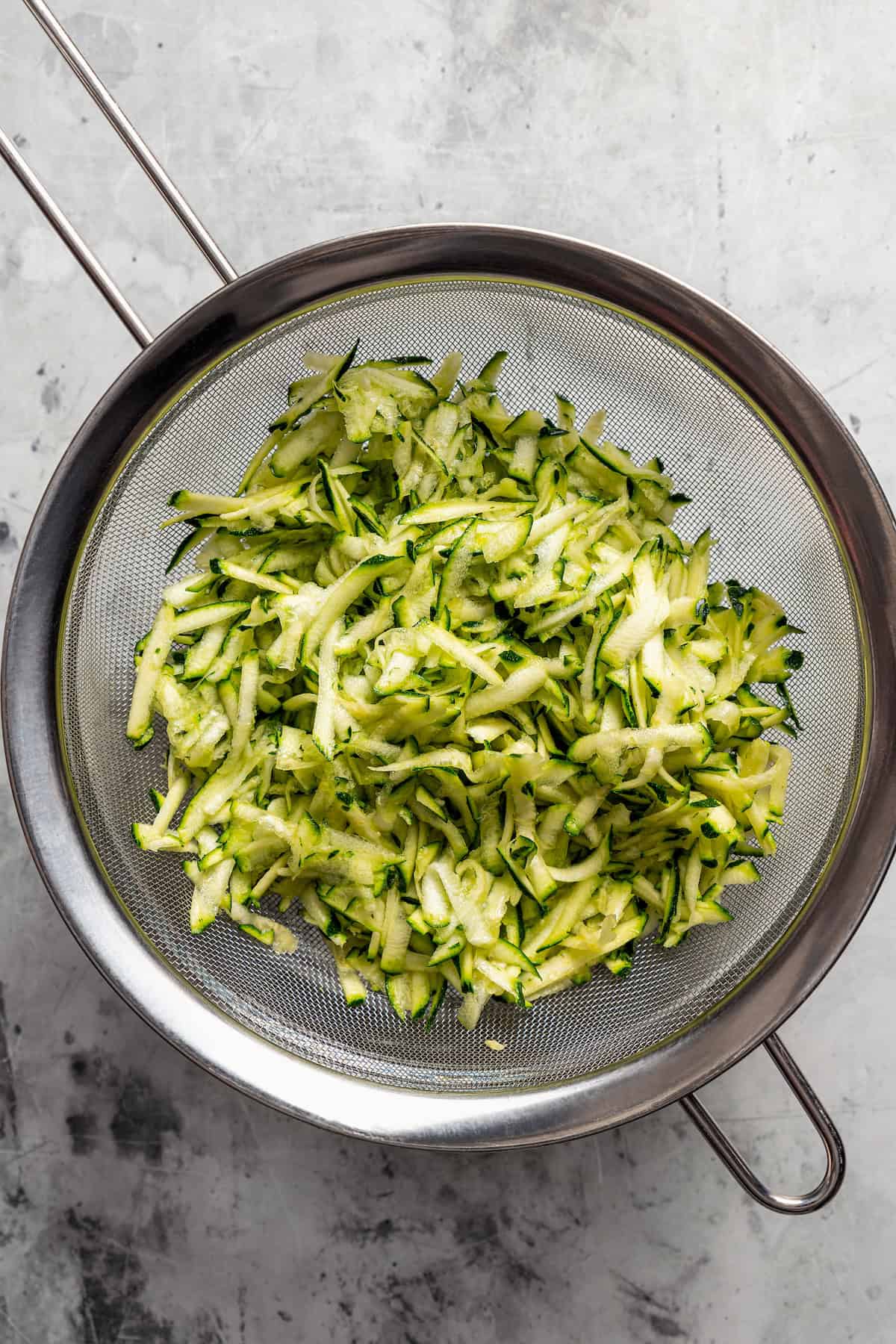 Salted zucchini straining in a mesh sieve.