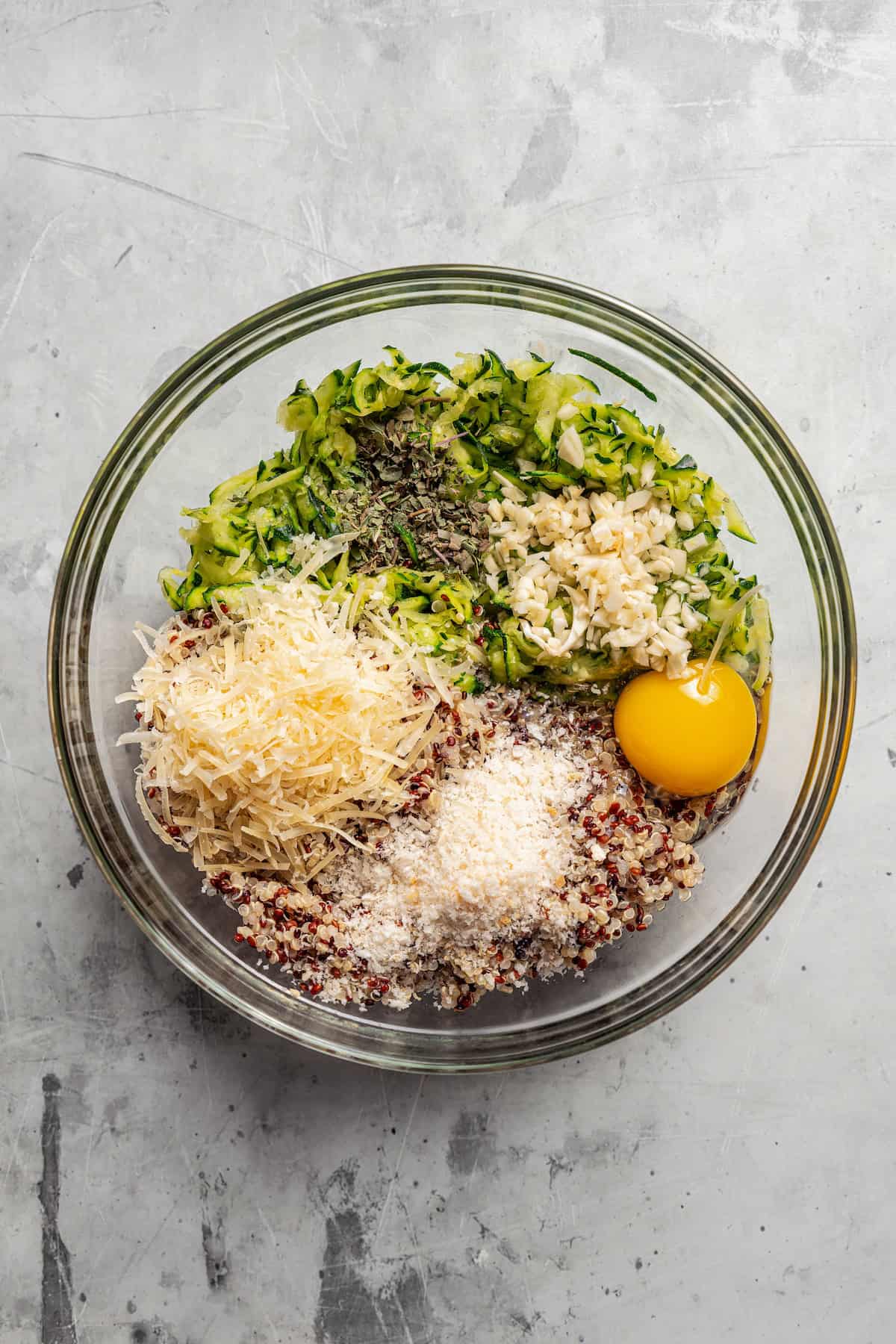 Quinoa zucchini fritter ingredients combined in a glass bowl.