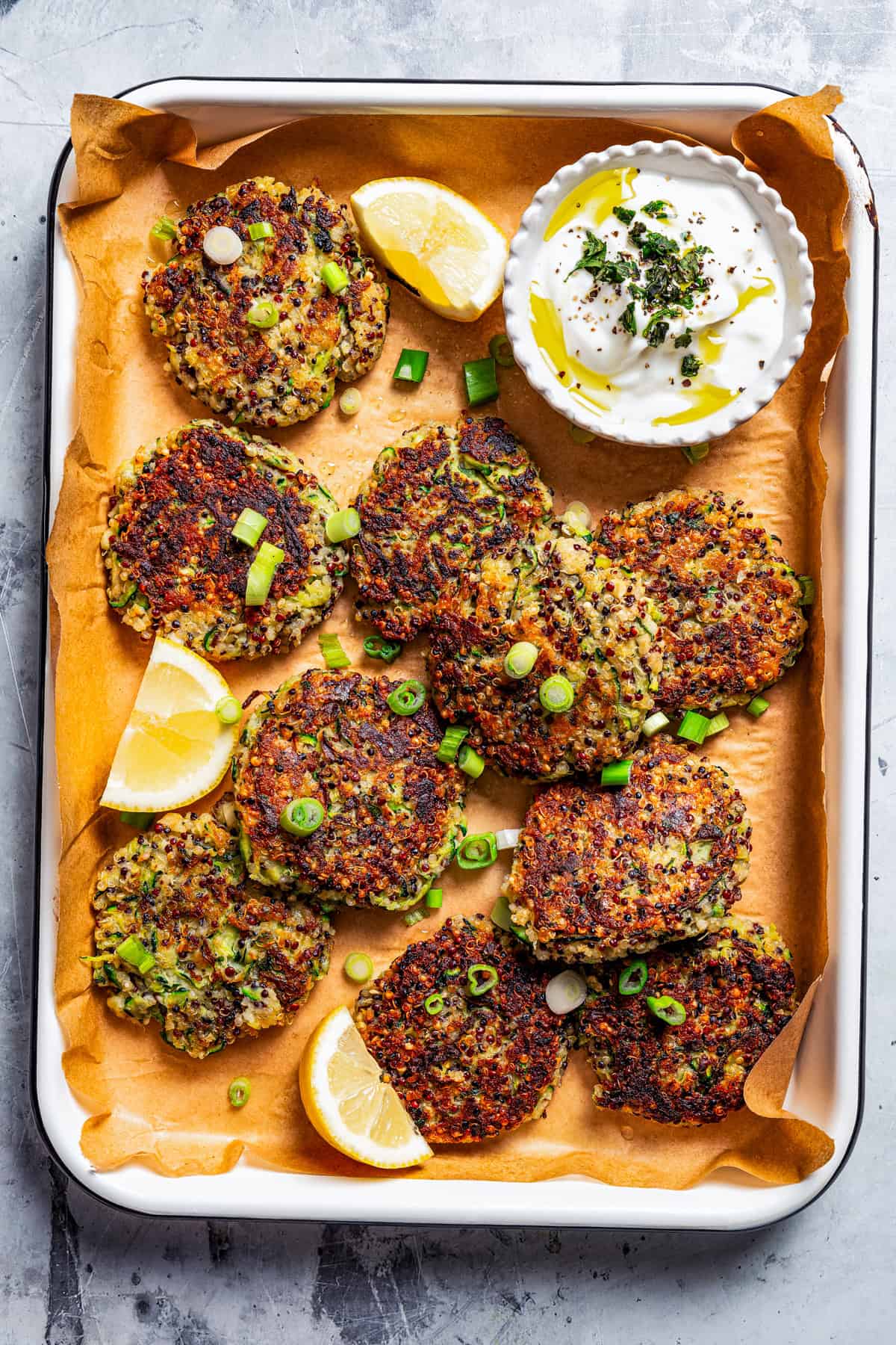 Zucchini fritters arranged on a parchment-lined baking sheet, with a bowl of dipping sauce to the side.