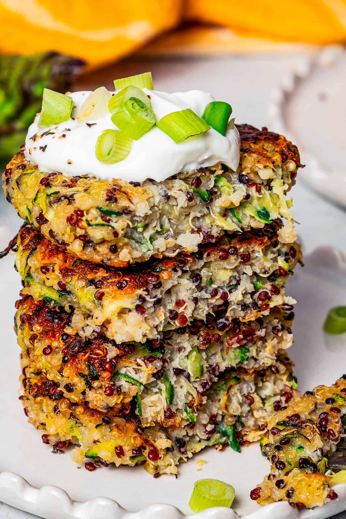 Zucchini fritters stacked on a plate, topped with yogurt, with a forkful resting on the plate.