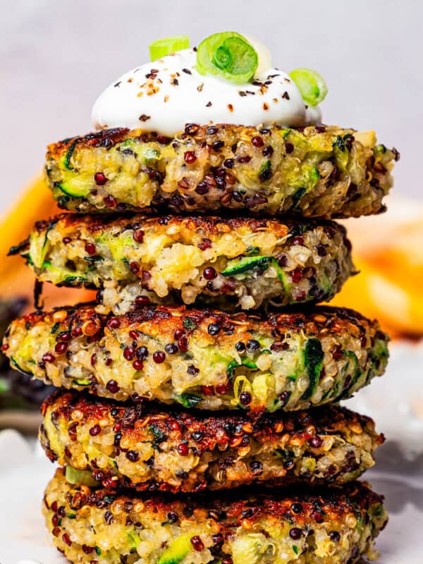 Five quinoa and zucchini fritters stacked on a plate and topped with a dollop of plain yogurt.