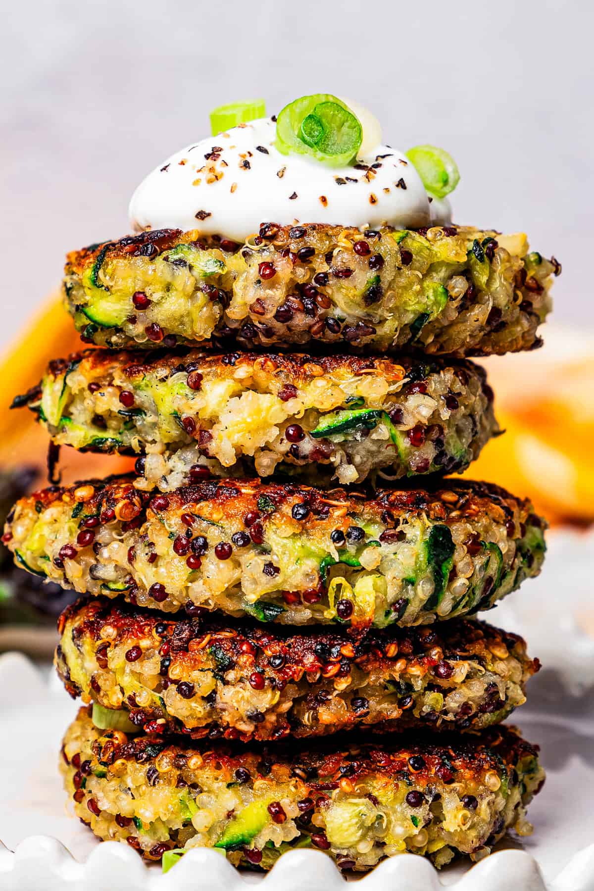 Five quinoa and zucchini fritters stacked on a plate and topped with a dollop of plain yogurt.