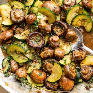 sliced zucchini and button mushrooms cooking in a stainless steel skillet