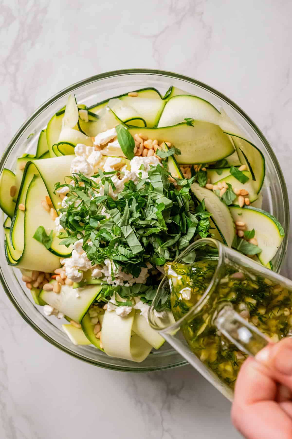 Salad dressing boing poured over a bowl of zucchini salad ingredients.