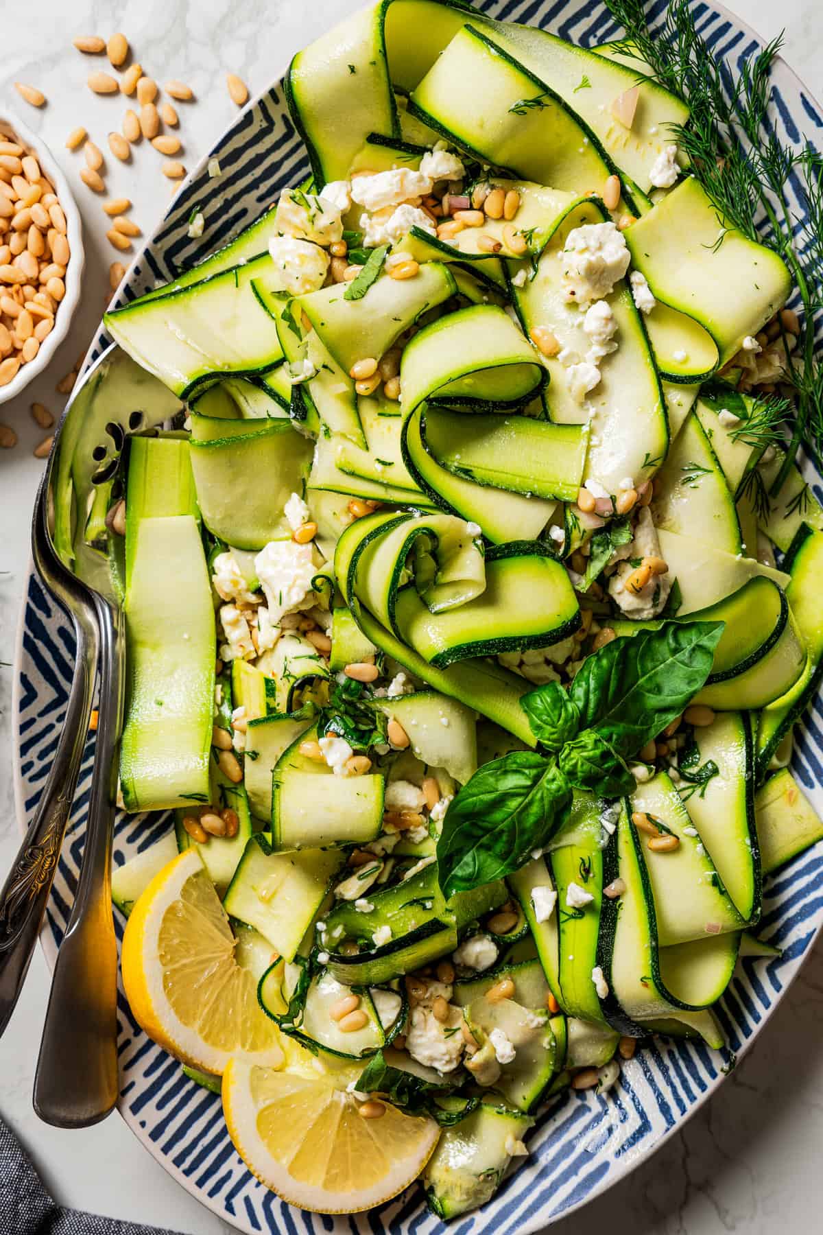 Overhead view of zucchini salad on a large platter garnished with fresh basil leaves and lemon wedges.