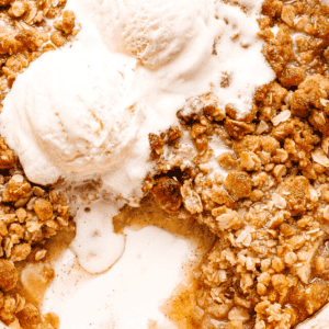 Baked Apple Crumble in a white baking dish, topped with two scoops vanilla ice cream.