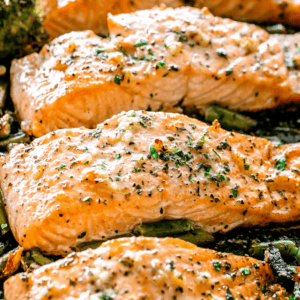 overhead shot of four baked salmon fillets on a sheet pan set on top of green vegetables.